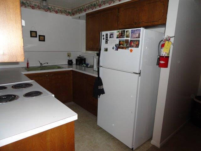 Kitchen, with white refrigerator, dark wood cupboards, white countertops at Crestview 457 East, unfurnished family housing.