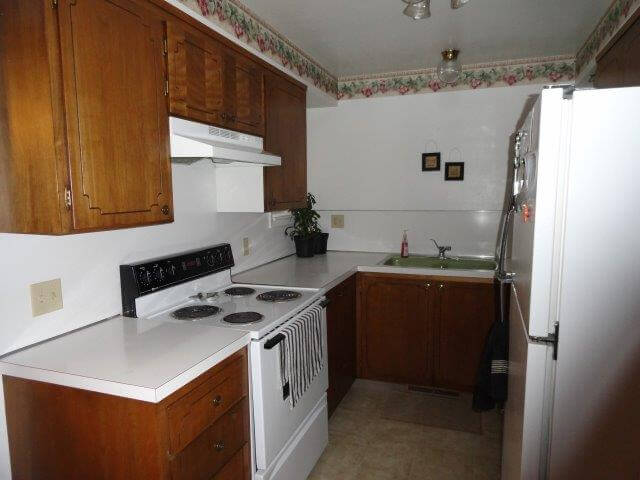 Kitchen, with white oven, dark wood cupboards, white countertops at Crestview 457 East, unfurnished family housing.