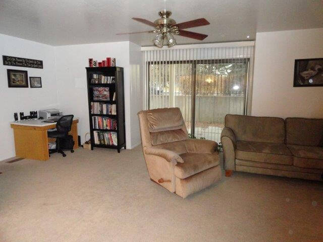Living room, with sliding patio doors, sofa, chair, desk, and bookshelves at Crestview 457 East, unfurnished family housing.