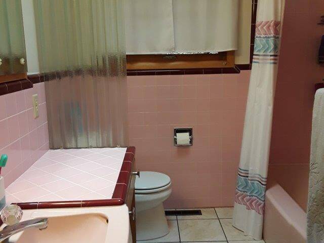 Bathroom 1 showing pink tile, wood vanity, toilet, window, and tub/shower.