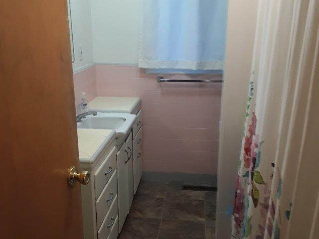 Bathroom with white cabinets and sink, pink tile, window, and tub/shower (toilet behind shower not showing).