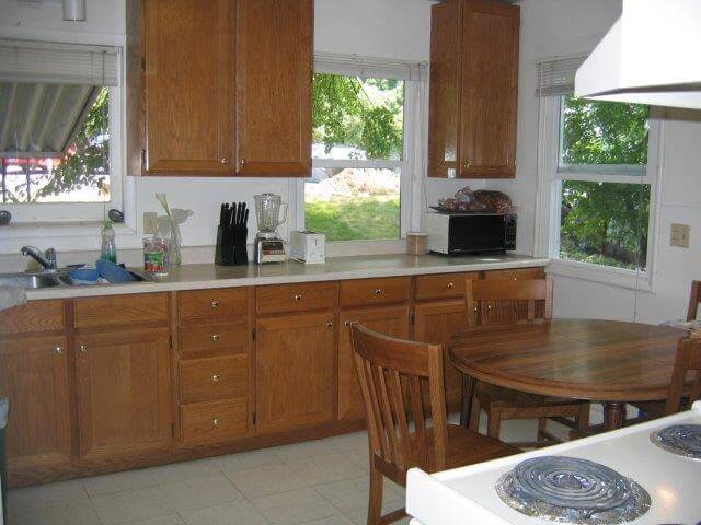 Kitchen with oak cabinets, off-white countertops, wood table w/ four chairs, white stove, and three windows.