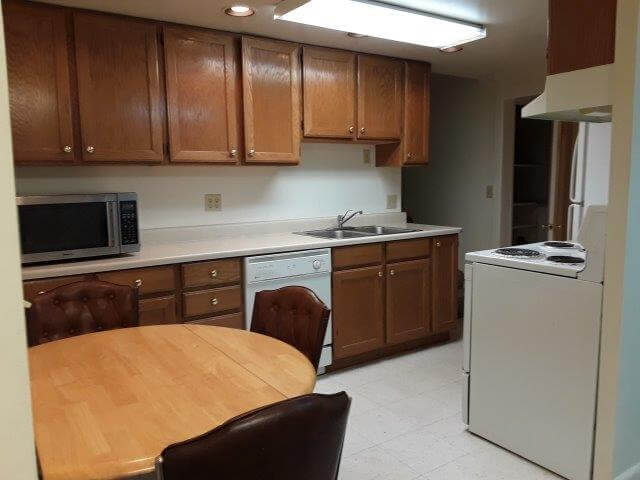 Kitchen showing oak cabinets, off-white countertops, wood table/chairs, microwave, dishwasher, oven and fridge.