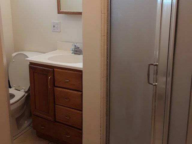 Small bathroom with toilet, oak vanity with white sink, and shower.