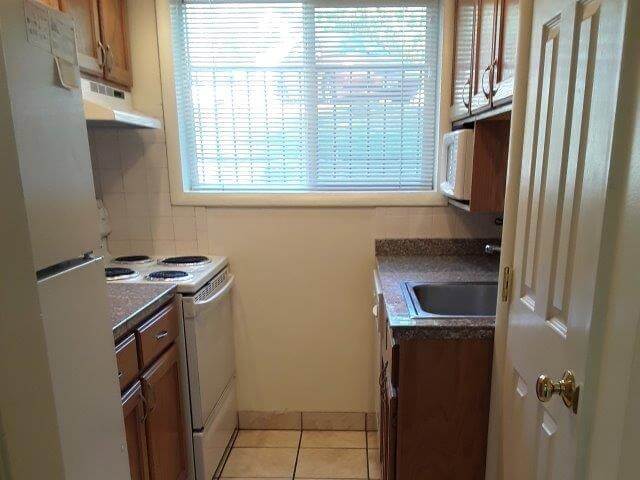 Small kitchen showing refrigerator, oak cabinets, granite countertops, oven, large window, microwave, dishwasher, and sink.