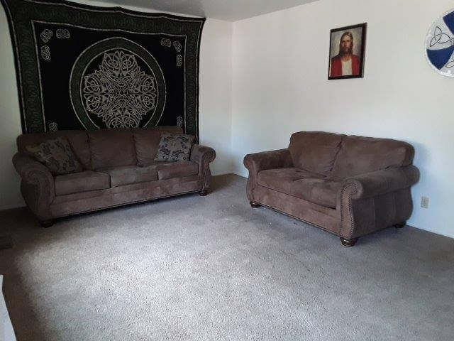Apartment living room with brown, leather-look sofa and loveseat; resident has decorated with wall hangings and framed art.