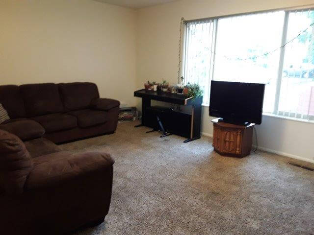 Apartment living room with brown microfiber sofa and loveseat, oak end table, and large window.